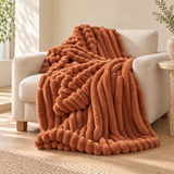 Caramel Ember bubble faux-fur throw on an oatmeal linen armchair. AI-styled scene based on supplier photography; colour and texture pending sample verification.