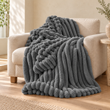 Charcoal Drape bubble faux-fur throw on an oatmeal linen armchair. AI-styled scene based on supplier photography; colour and texture pending sample verification.