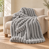 Pebble Mist bubble faux-fur throw on an oatmeal linen armchair. AI-styled scene based on supplier photography; colour and texture pending sample verification.